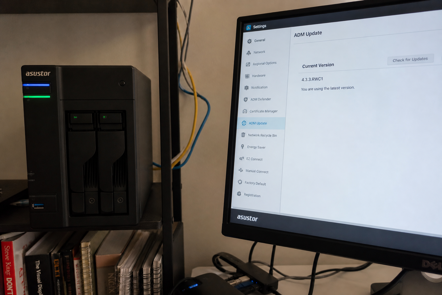 ASUSTOR NAS on a shelf next to a monitor showing ADM Update at 4.3.3.RWC1