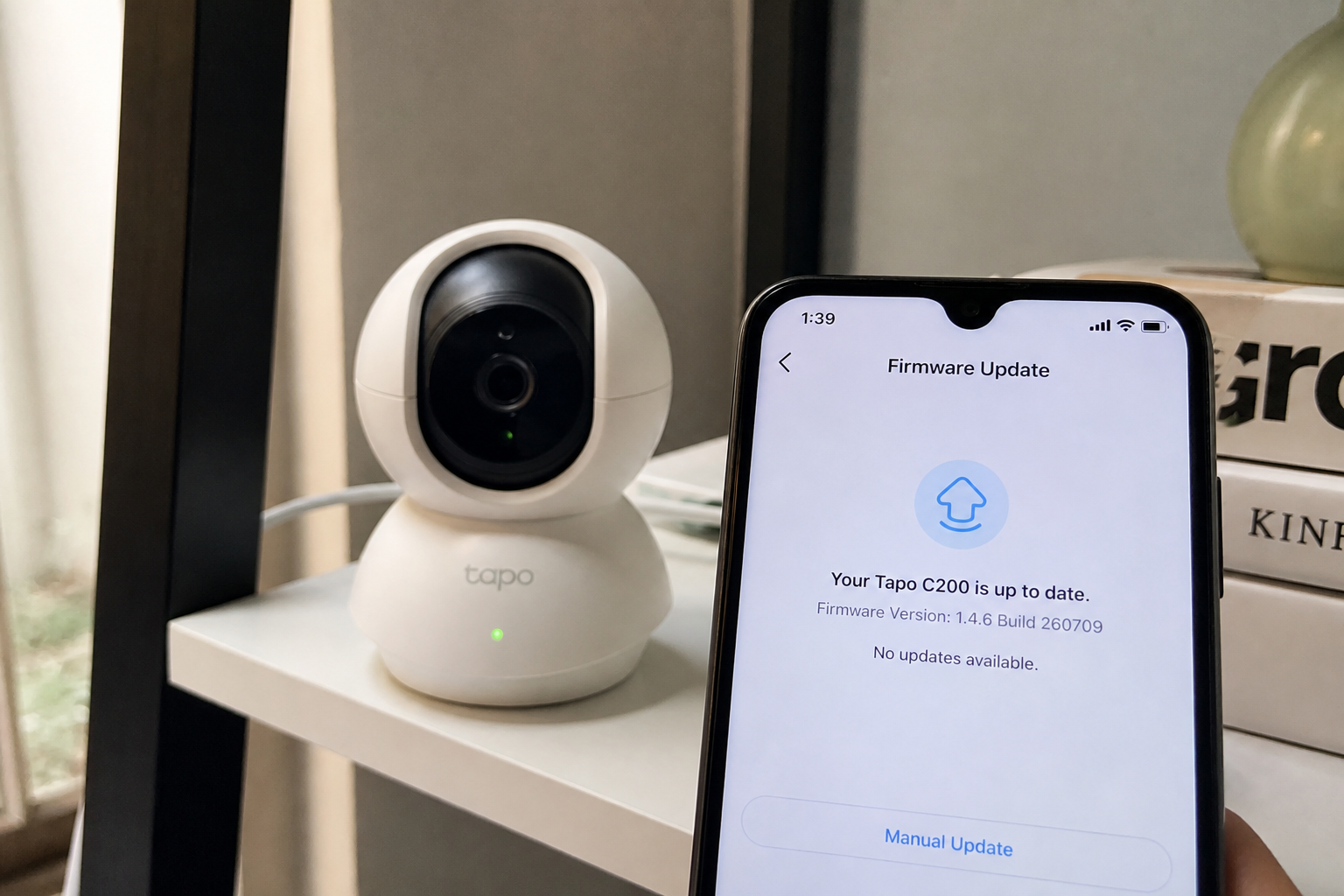 Tapo C200 on a shelf next to a phone showing Firmware Version 1.4.6 Build 260709