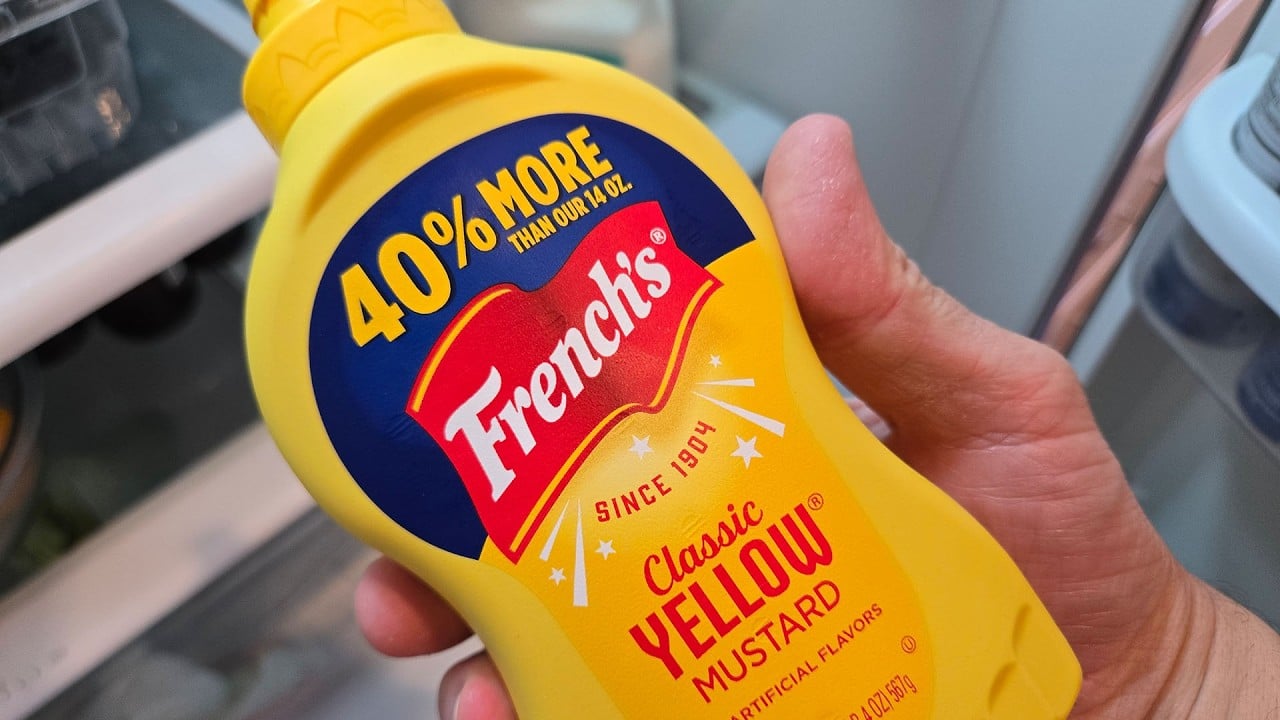 Never Put Mustard in Your Fridge Scam Exposed: How the Clickbait Works 2 Bottle of yellow mustard held in front of an open refrigerator